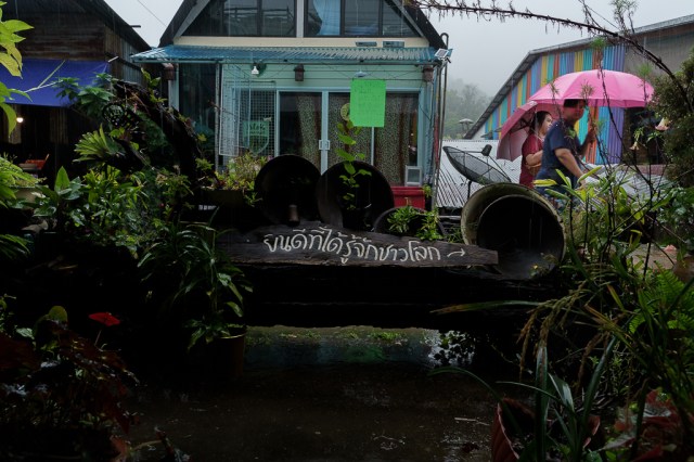 ชายหญิงเดินกางร่มกลางฝนผ่านป้ายหน้าร้าน